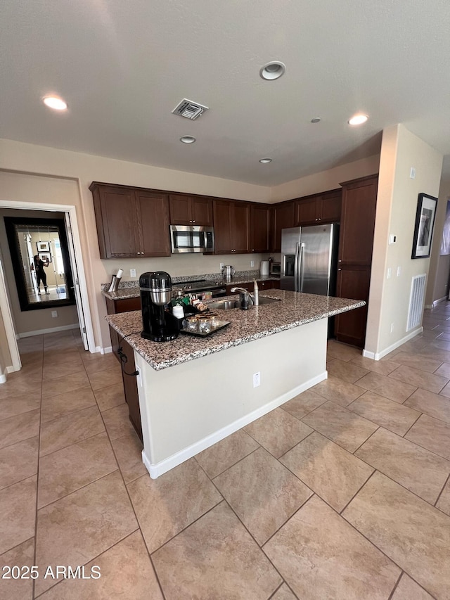 kitchen with stainless steel appliances, a center island with sink, light stone countertops, and sink