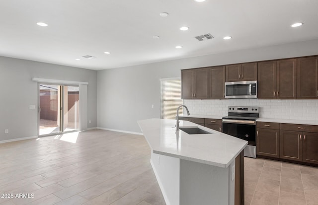 kitchen with tasteful backsplash, appliances with stainless steel finishes, sink, and a kitchen island with sink