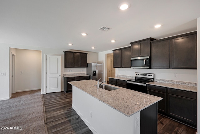 kitchen with light stone counters, an island with sink, sink, dark hardwood / wood-style floors, and appliances with stainless steel finishes