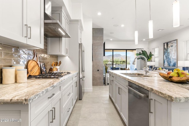 kitchen featuring stainless steel appliances, wall chimney exhaust hood, an island with sink, and decorative light fixtures