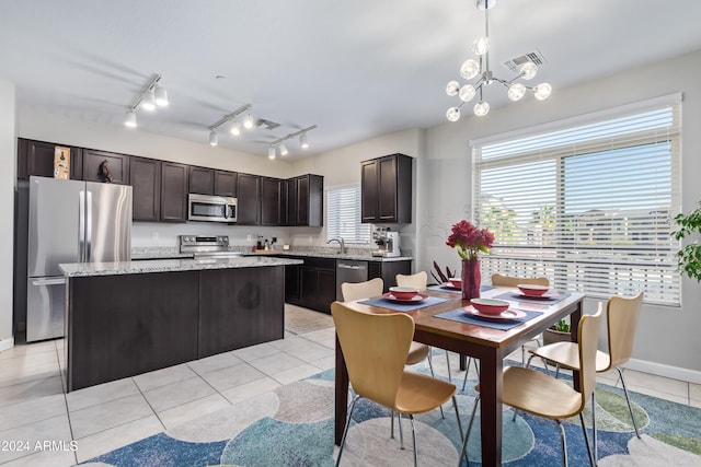 kitchen with appliances with stainless steel finishes, light tile patterned floors, a notable chandelier, a kitchen island, and hanging light fixtures