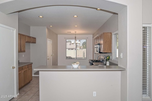 kitchen featuring pendant lighting, stove, an inviting chandelier, light tile patterned flooring, and kitchen peninsula