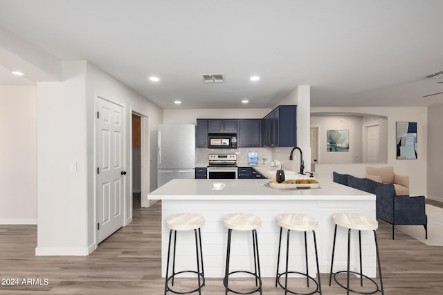 kitchen featuring tasteful backsplash, appliances with stainless steel finishes, light hardwood / wood-style flooring, and a kitchen breakfast bar