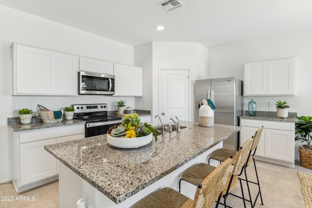 kitchen with a breakfast bar area, visible vents, appliances with stainless steel finishes, a sink, and light stone countertops