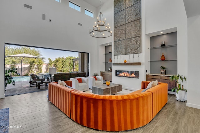 2652 E Pelican Ct, Gilbert, AZ 85297 - living room with a high ceiling, a glass covered fireplace, wood finished floors, a chandelier, and built in shelves