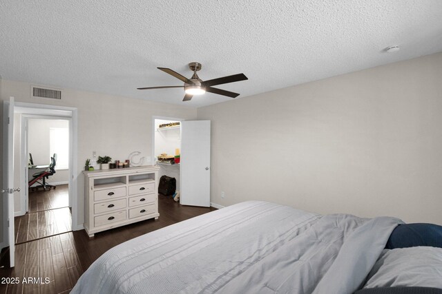 bedroom with a spacious closet, visible vents, baseboards, ceiling fan, and dark wood-style floors