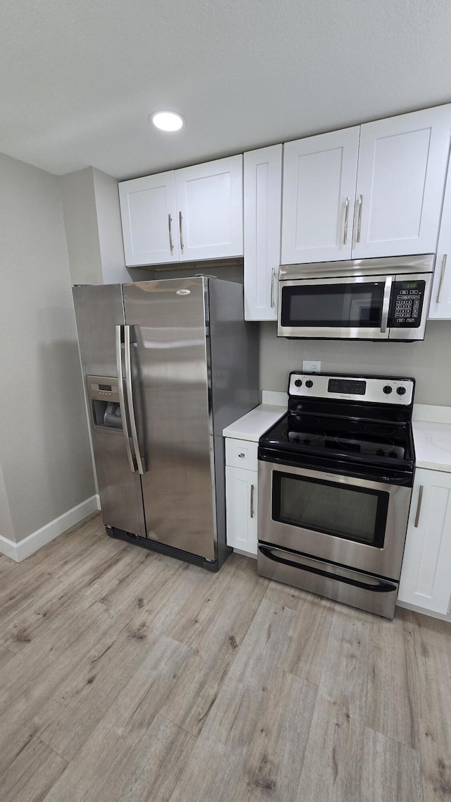 kitchen with baseboards, light wood-style flooring, light countertops, white cabinets, and appliances with stainless steel finishes