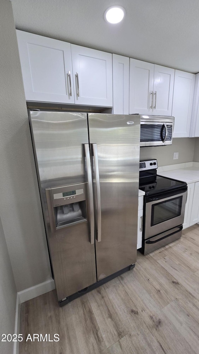 kitchen with white cabinetry, stainless steel appliances, light countertops, and light wood finished floors