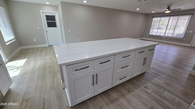 kitchen with white cabinetry, light wood-style flooring, a center island, light stone countertops, and recessed lighting