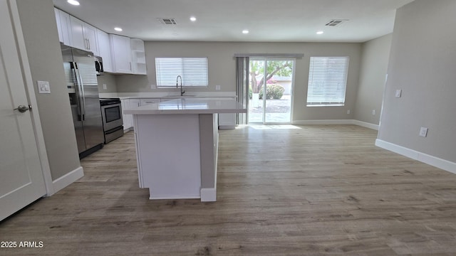 kitchen with appliances with stainless steel finishes, light wood finished floors, open shelves, and white cabinets