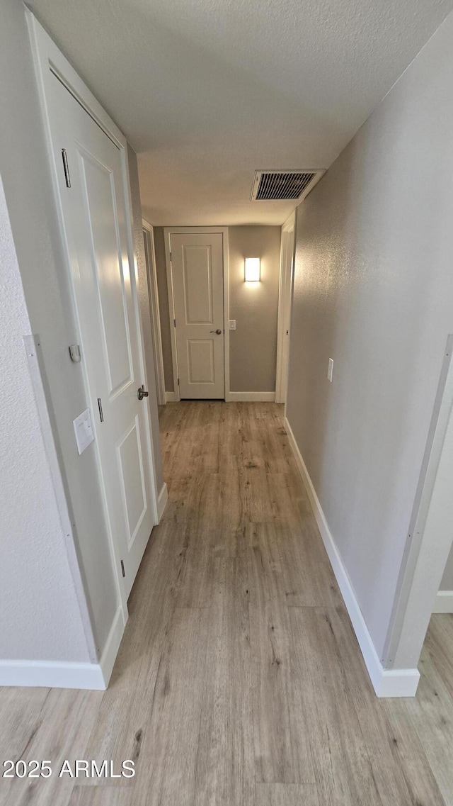 corridor with baseboards, visible vents, and light wood-style flooring