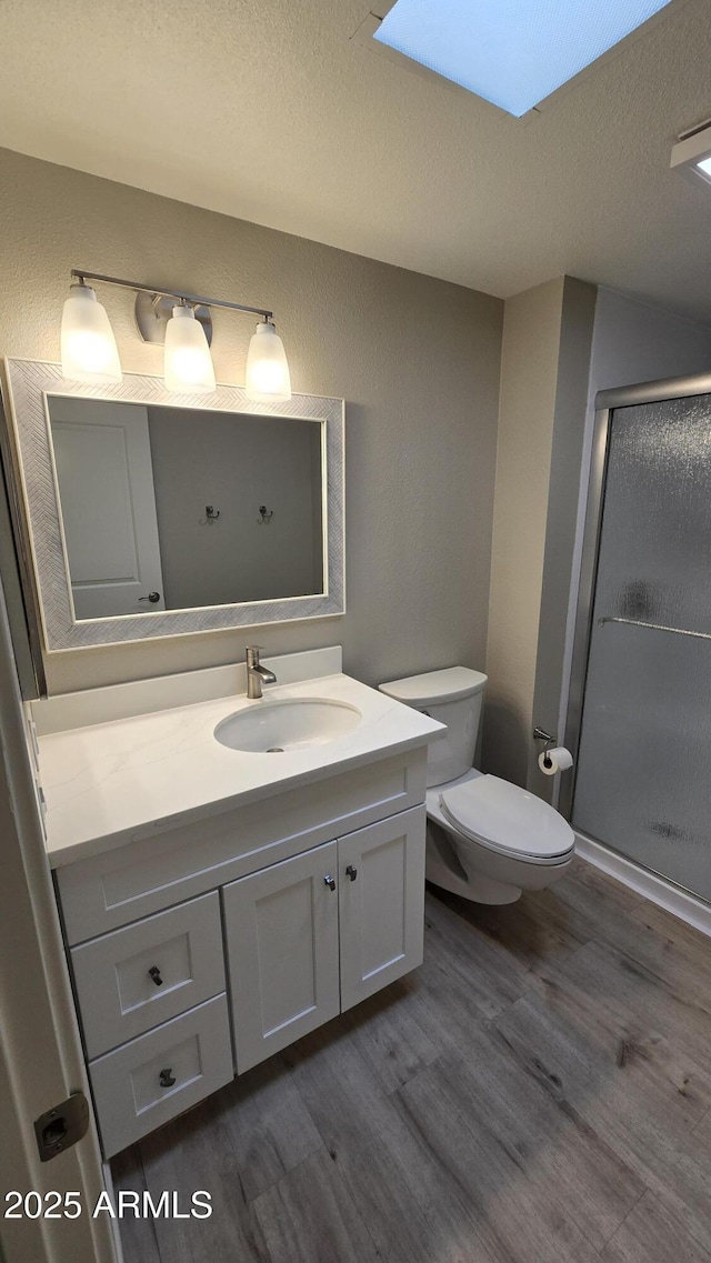 bathroom featuring vanity, toilet, a stall shower, a textured ceiling, and wood finished floors