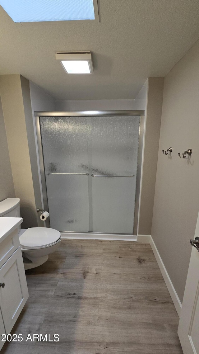 bathroom with wood finished floors, toilet, vanity, a stall shower, and a textured ceiling