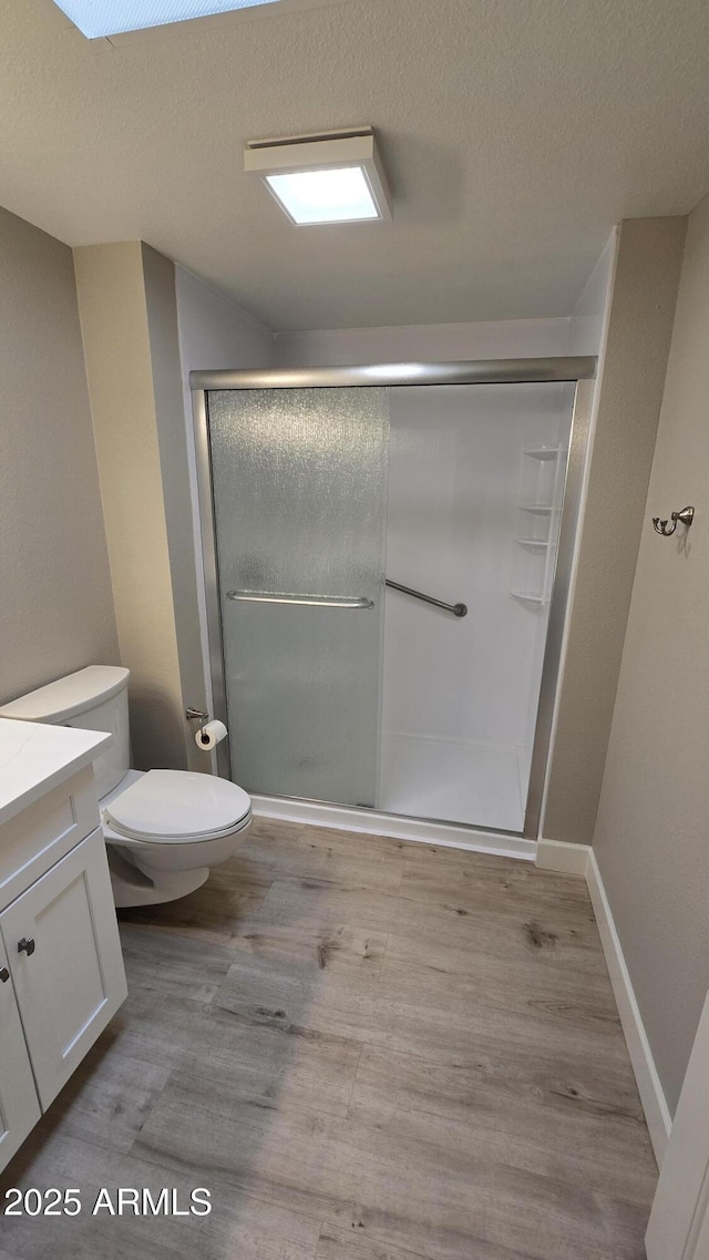 bathroom with a textured ceiling, a shower stall, toilet, wood finished floors, and vanity
