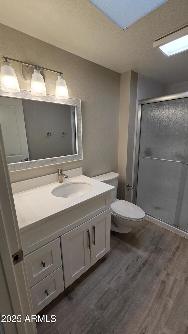 bathroom with wood finished floors, a shower stall, toilet, and vanity
