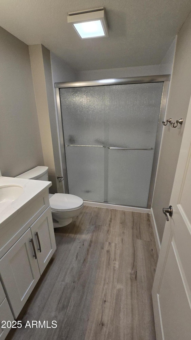 full bathroom featuring toilet, wood finished floors, a shower stall, and vanity