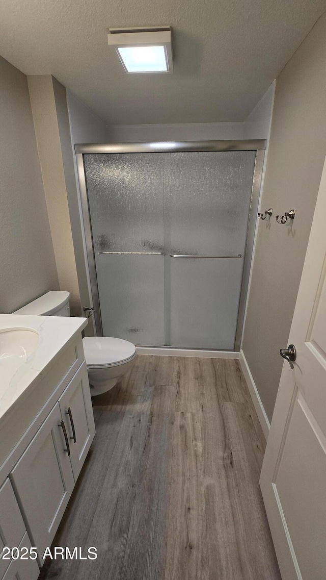 bathroom featuring a textured ceiling, a stall shower, toilet, wood finished floors, and vanity