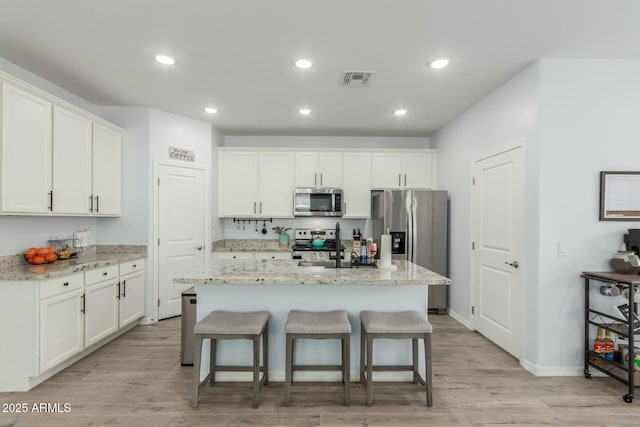 kitchen with white cabinetry, stainless steel appliances, and an island with sink