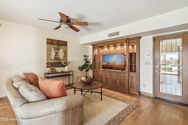 living area featuring a ceiling fan, baseboards, visible vents, and light wood finished floors