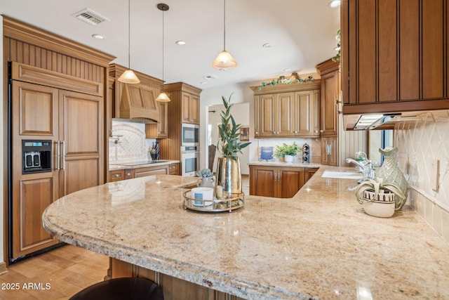 kitchen with custom exhaust hood, visible vents, a sink, built in appliances, and a peninsula