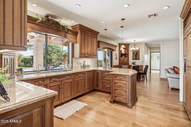 kitchen featuring a peninsula, light stone counters, visible vents, and brown cabinets