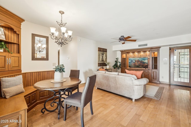 dining space with a wainscoted wall, visible vents, light wood-style flooring, and ceiling fan with notable chandelier