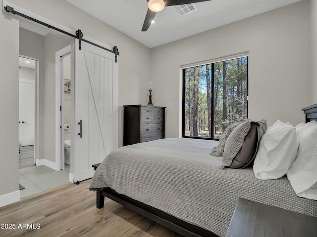 1137 Timbernook Xing, Williams, AZ 86046 - bedroom featuring a barn door, light wood finished floors, ceiling fan, ensuite bath, and baseboards