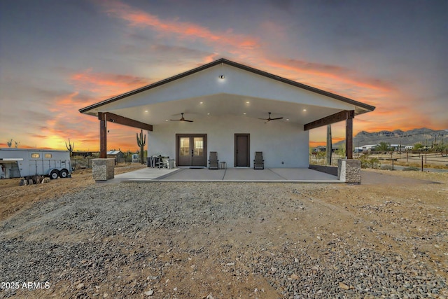 back of house at dusk with ceiling fan, a patio, a mountain view, and stucco siding