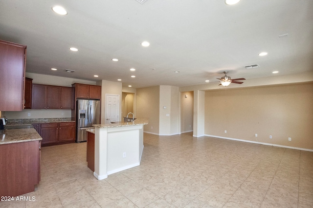 kitchen with ceiling fan, stainless steel fridge, light tile floors, sink, and a kitchen island with sink