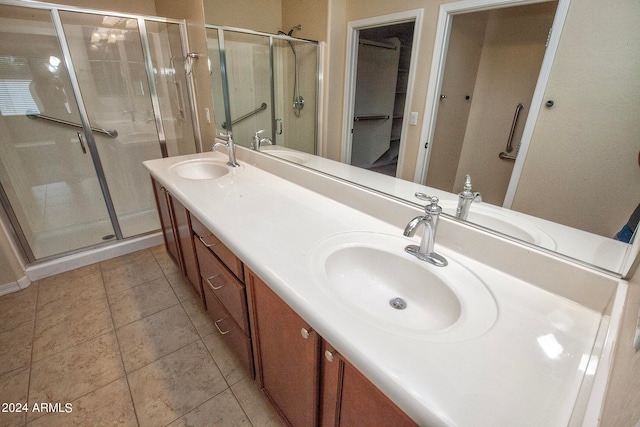 bathroom with a shower with shower door, large vanity, double sink, and tile floors