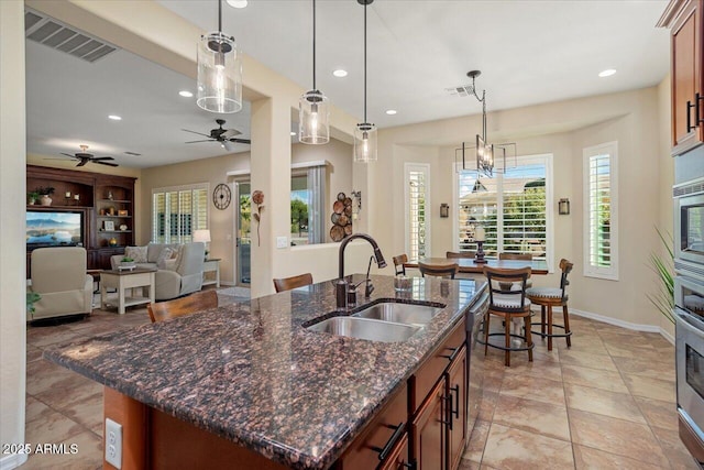 kitchen with pendant lighting, sink, appliances with stainless steel finishes, dark stone countertops, and an island with sink