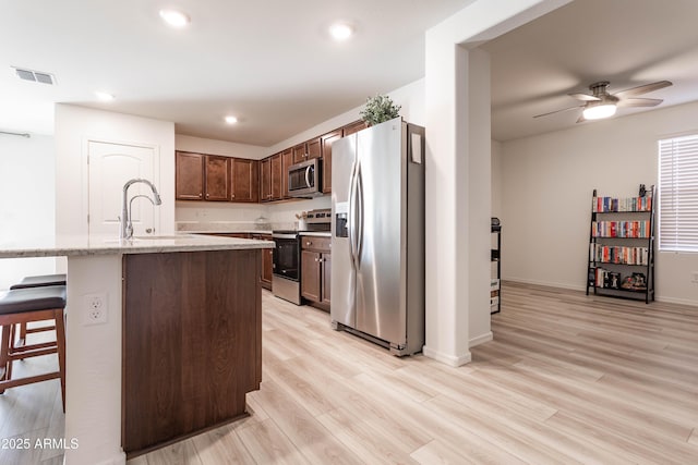 kitchen with a kitchen bar, sink, light wood-type flooring, an island with sink, and stainless steel appliances