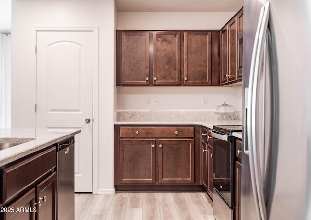 kitchen featuring dark brown cabinetry, light stone counters, light hardwood / wood-style floors, and appliances with stainless steel finishes