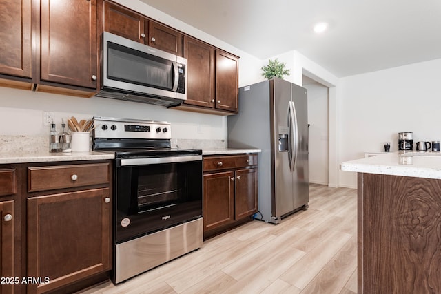 kitchen with dark brown cabinetry, light stone counters, light hardwood / wood-style floors, and appliances with stainless steel finishes