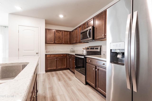 kitchen with light stone counters, appliances with stainless steel finishes, dark brown cabinets, and light wood-type flooring