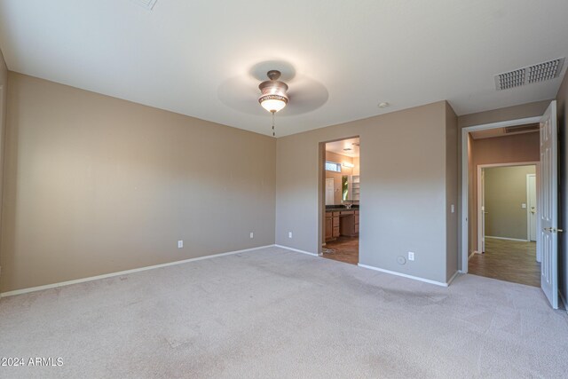 unfurnished bedroom featuring light colored carpet, ceiling fan, and ensuite bathroom