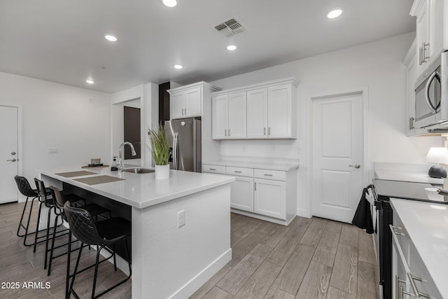 kitchen featuring a kitchen island with sink, sink, white cabinetry, and appliances with stainless steel finishes