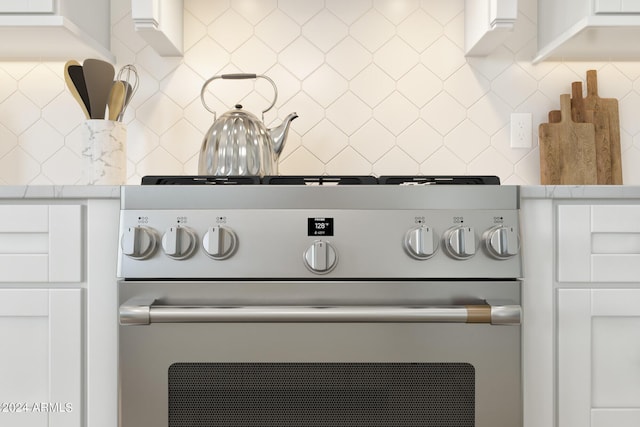 details featuring decorative backsplash, range, and white cabinetry