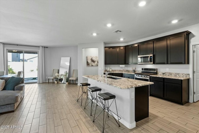 kitchen with sink, a kitchen breakfast bar, light stone countertops, a center island with sink, and appliances with stainless steel finishes