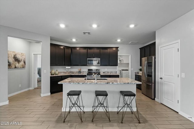 kitchen featuring light stone countertops, stainless steel appliances, an island with sink, a breakfast bar area, and sink