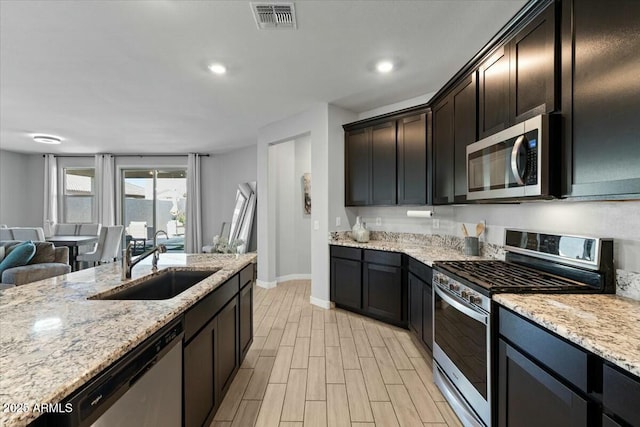 kitchen with light stone counters, sink, stainless steel appliances, light hardwood / wood-style floors, and dark brown cabinetry