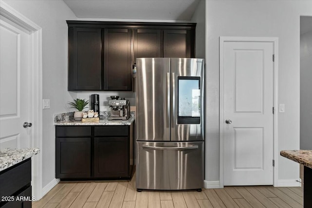 kitchen with dark brown cabinets, light stone counters, and stainless steel fridge