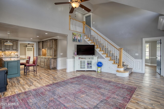 living room with hardwood / wood-style flooring, ceiling fan, ornamental molding, and high vaulted ceiling