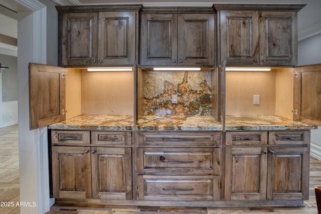 bar featuring light stone counters, dark brown cabinets, tasteful backsplash, and ornamental molding