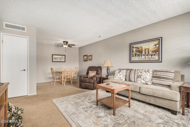 living room with a textured ceiling, light carpet, and ceiling fan