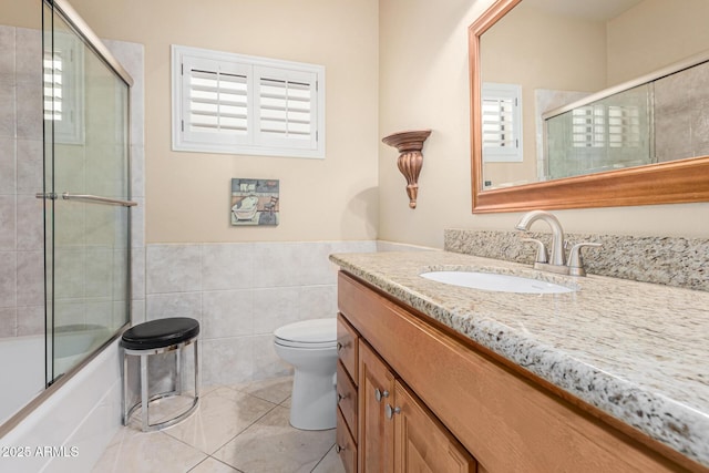 full bathroom with combined bath / shower with glass door, tile walls, tile patterned flooring, vanity, and toilet