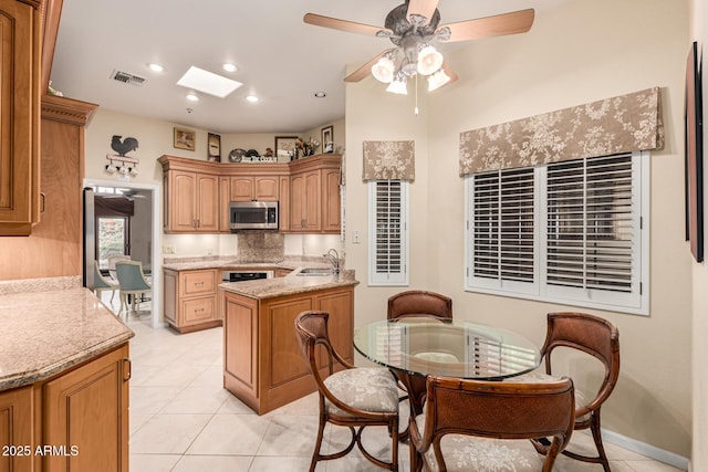 kitchen with sink, appliances with stainless steel finishes, a skylight, tasteful backsplash, and light stone countertops