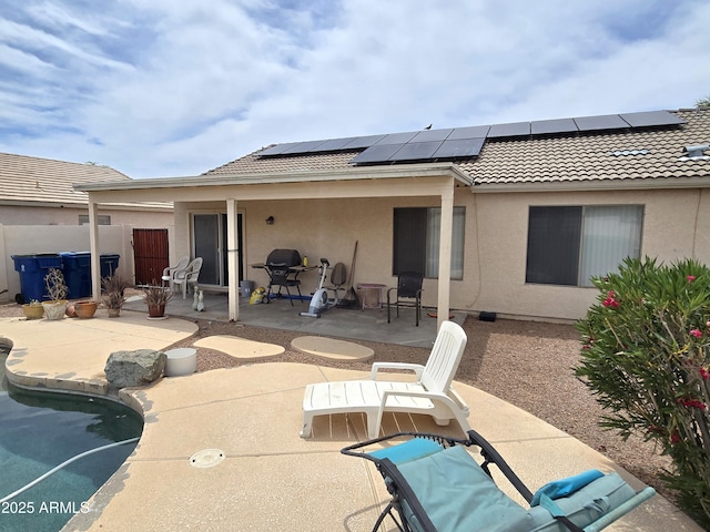 rear view of house featuring a patio, a tiled roof, stucco siding, roof mounted solar panels, and an outdoor pool