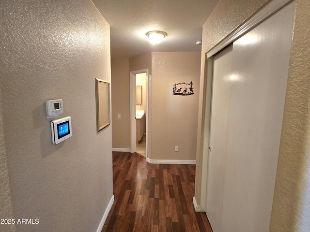 hallway featuring wood finished floors, a textured wall, baseboards, and a textured ceiling