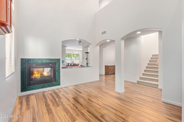 unfurnished living room featuring a towering ceiling, light wood-type flooring, and a tiled fireplace